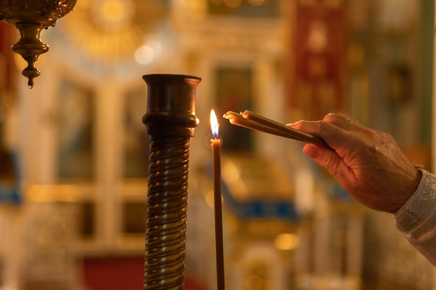 Chiesa ortodossa cristianesimo mano del sacerdote che accende candele accese nella tradizionale chiesa ortodossa