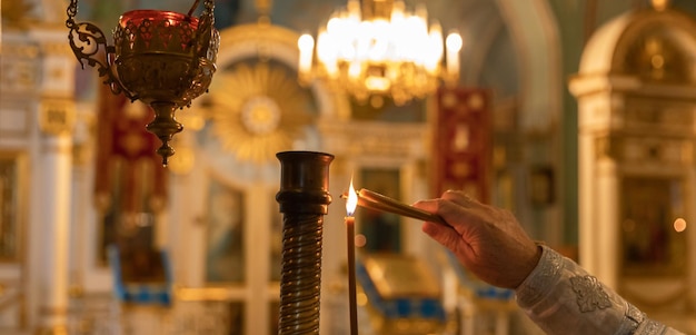 Orthodox church christianity hand of priest lighting burning candles in traditional orthodox church