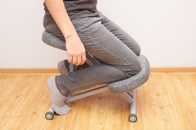 Ортопедический эргономичный стул на коленях крупным планом на фоне стены дома, здоровье спины