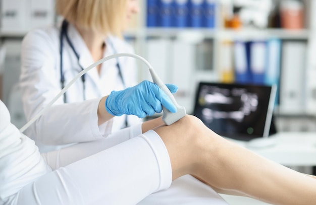 Orthopedisch arts maakt echografie van de knie van de patiënt in kantoor Jonge vrouw ondergaat echografie van botten en gewrichten van benen in de kliniek