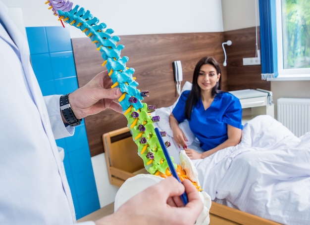 病院で患者に脊椎モデルを示す整形外科医