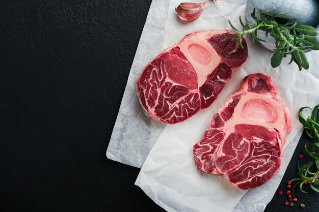 Photo osso buco raw steak meat barbecue meat raw fresh cross cut veal shank and seasonings pepper rosemary thyme and salt on dark background beef leg slice italian menu top view