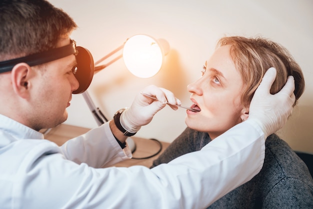 Otolaryngologist examines woman's throat with medical spatula.