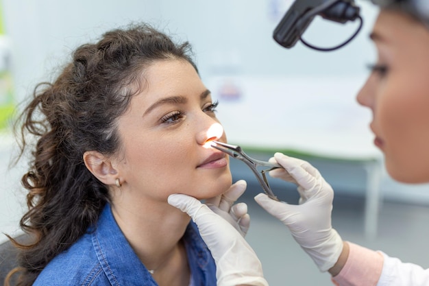 Otolaryngology concept Positive woman otorhinolaryngologist checking nose with otoscope of his patient at hospital Nasal congestion sinusitis allergy concept Female patient at modern ENT clinic