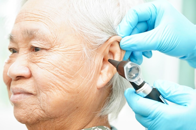 Otolaryngoloog of HOO-arts die het oor van een oudere patiënt met gehoorverlies met een otoscoop onderzoekt