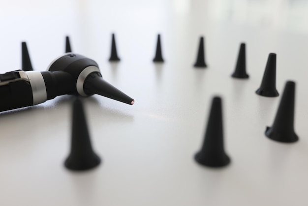 Otoscope for ear examination surrounded by black funnels on white table in clinic professional