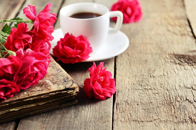 Oud boek met mooie rozen en kopje koffie op houten tafel close-up