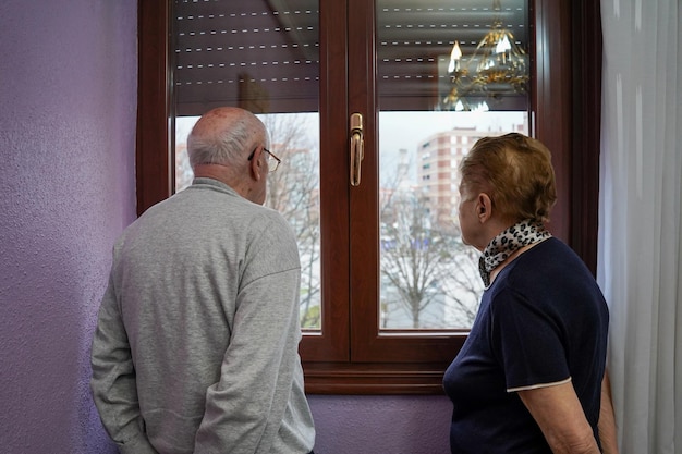 Foto oud stel kijkt naar het raam in huiseenzaamheid bij ouderen