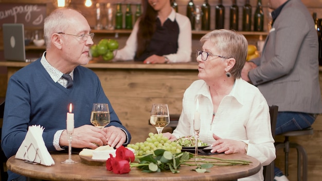 Oud stel zit aan tafel in een restaurant en drinkt wijn. haar verhalen vertellen. ontspannen paar. vrolijk paar. romantisch paar.