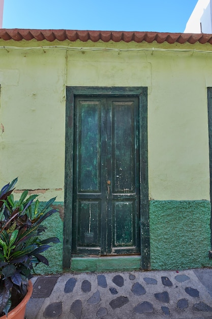 Oud verlaten huis of huis met een verweerde groene muur en een gebroken houten deur Vintage en oud woongebouw gebouwd in een traditionele architecturale stijl of ontwerp op een geplaveide straat