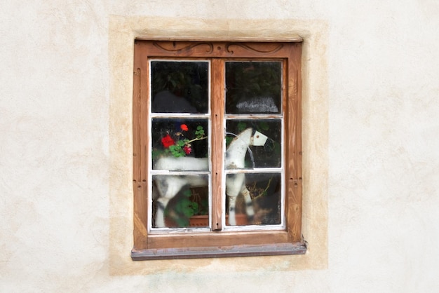 Oud wit speelgoedpaard buiten het raam met een houten frame op een achtergrond van de witte stenen muur