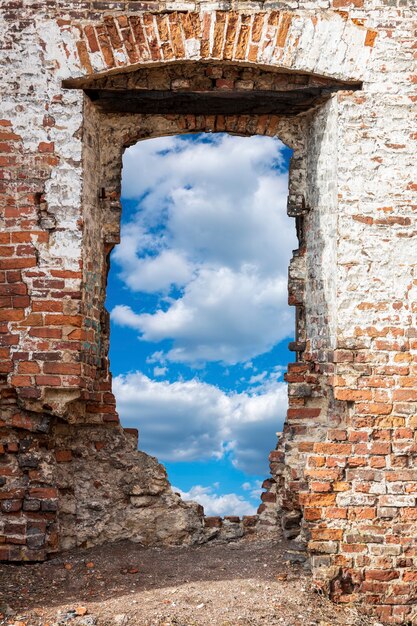 Oude bakstenen muur met een gat tegen de blauwe lucht met wolken. Hoge kwaliteit foto