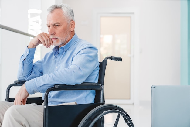 Oude blanke man zittend op rolstoel voelt zich eenzaam en depressief binnenshuis