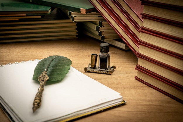 Oude boeken in wanorde gestapeld een oude pen met zijn inkt en een notitieblok op een oude houten tafel