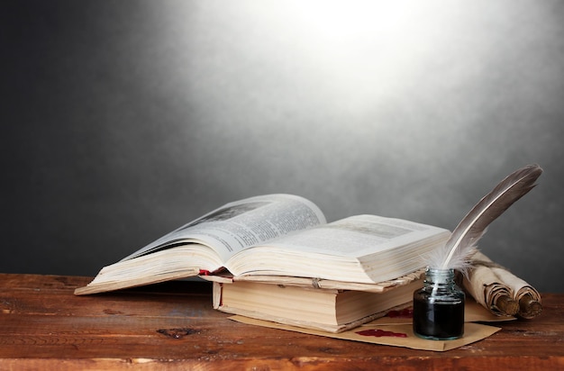 Oude boeken scrollen veren pen en inktpotje op houten tafel op grijze achtergrond