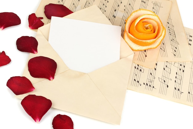 Foto oude envelop met blanco papier en gedroogde rozenblaadjes op muziekbladen close-up