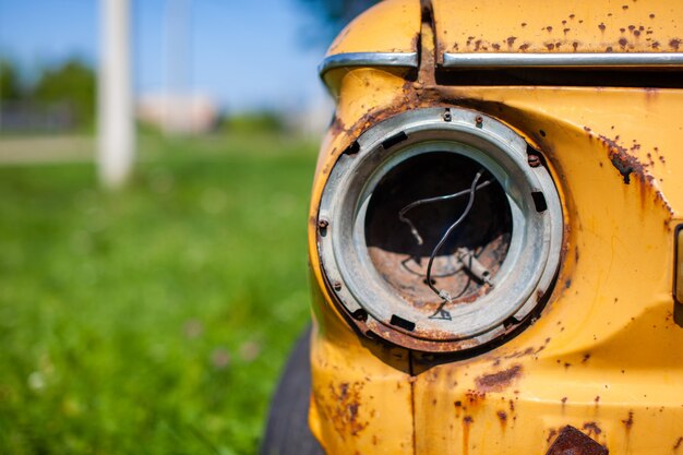 Oude gele vernielde auto in vintage stijl. Verlaten roestige gele auto. Close-up van de koplampen van het vooraanzicht van een roestige, kapotte, verlaten auto in de buurt van het huis. Concept van verlaten gebruikte auto.