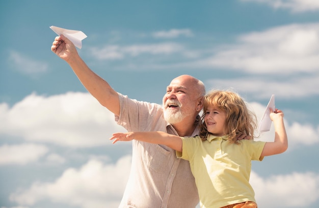 Oude grootvader en jong kind kleinzoon met speelgoed papier vliegtuig tegen zomer hemel achtergrond kind