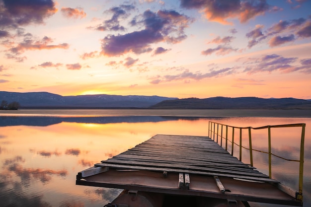 Foto oude houten pier op het bergmeer bij zonsondergang. wolken en hun reflecties in het wateroppervlak. smeltend ijs op het meer in het voorjaar.