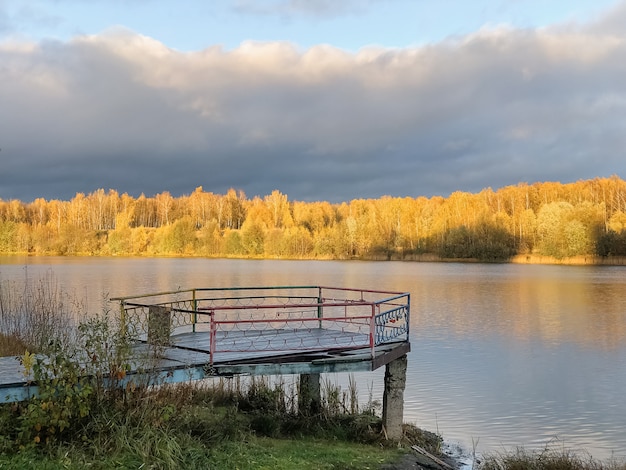Oude houten pier over stilstaand meerwater met herfstgele bosbomen aan de horizon