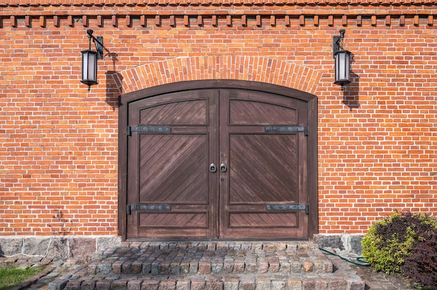 Oude houten poorten met ijzeren lussen, granieten stenen trappen en lampen aan de zijkanten in de rode bakstenen muur, close-up