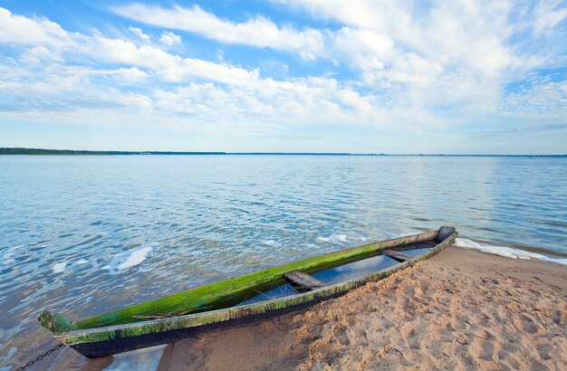 Oude houten vissersboot overstromingen in de buurt van de oever van het meer en de zomer hemel achter (Svityaz, Oekraïne)