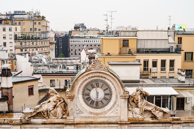 Oude klok op het dak van het huis met beelden aan de zijkanten milaan italië