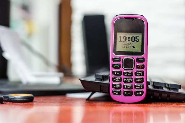 Oude knop mobiele telefoon roze kleur op het bureau in de buurt van een computertoetsenbord Klok en indicatoren op het zwart-wit scherm