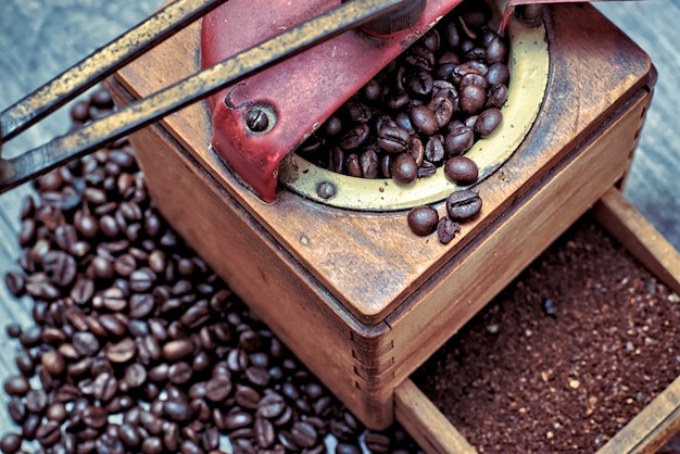 Oude koffiemolen met grondkoffie, koffiebonen op een houten achtergrond.