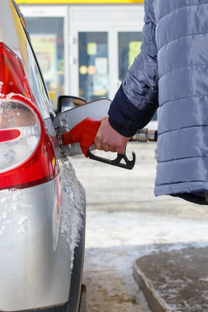 Oude man hand in blauwe warme jas tanken grijze metalen auto op tankstation overdag close-up met selectieve focus