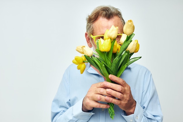 Oude man in een blauw shirt met een boeket bloemen lichte achtergrond