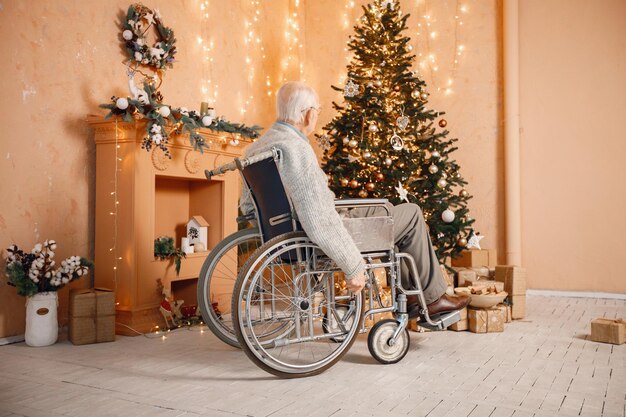 Oude man in een rolstoel die alleen bij de kerstboom zit