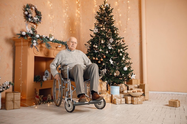 Oude man in een rolstoel die alleen bij de kerstboom zit