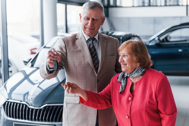 Oude man in formele kleding die vrouw ondersteunt bij het kiezen van een auto.
