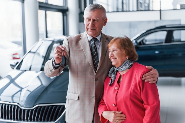 Oude man in formele kleding die vrouw ondersteunt bij het kiezen van een auto.