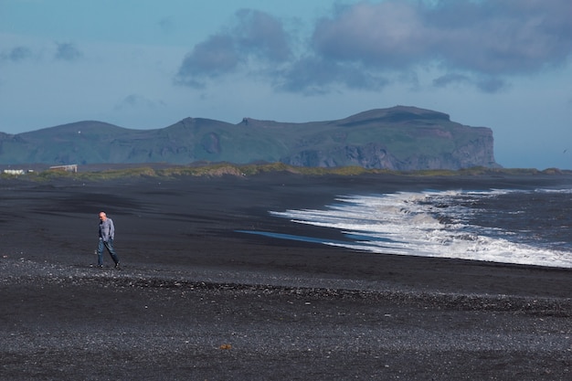 Oude man lopen op het zwarte zand van een strand in ijsland