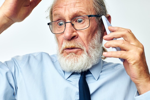 Oude man met telefoon geschokt in studio op witte achtergrond