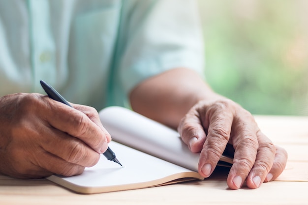 oude man schrijven op lege notitieblok pagina met zwarte inkt pen