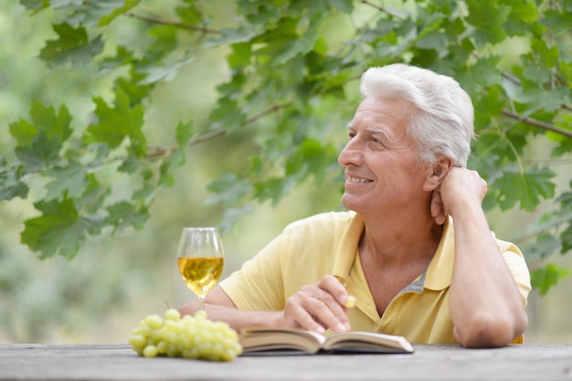 Oude man zit aan een tafel, drinkt wijn en leest een boek