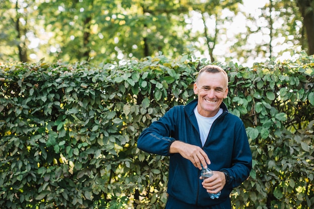 Oude mens die terwijl in hand het houden van een waterfles glimlacht