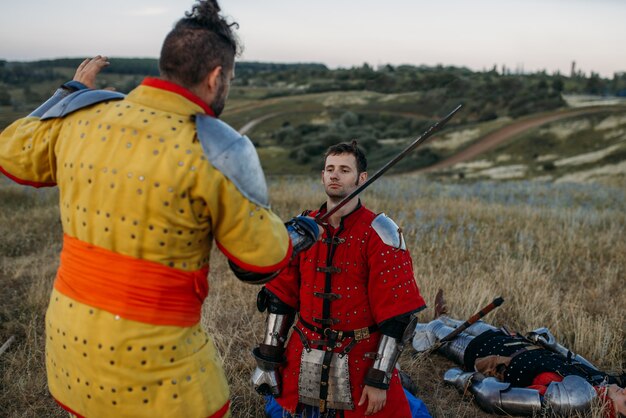 Oude middeleeuwse ridder in harnas treft voorbereidingen om het hoofd af te snijden, grote strijd. Gepantserde oude krijger in harnas poseren in het veld