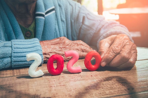 Foto oude persoonshanden die nummer 2020 op houten lijst houden. concept: de 2020 oudere wereldbevolking groeit dramatisch.
