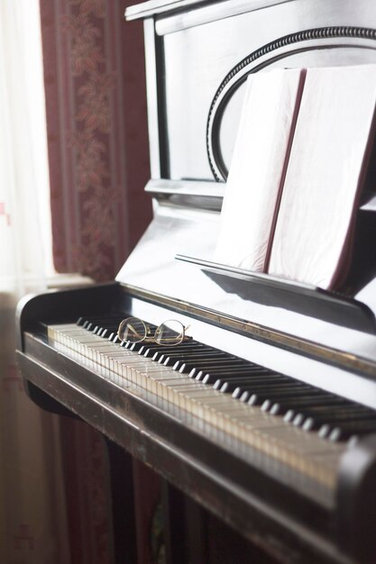 Oude piano met bladmuziek en bril liggend op het toetsenbord, close-up