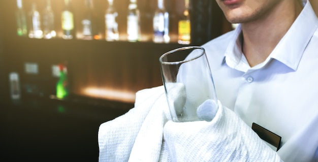 Foto oude pub met barman die het glas schoonmaakt met een witte handdoek op de achtergrond. lege naamplaatjesbadge op het overhemdsuniform. barman op zijn werkplek.