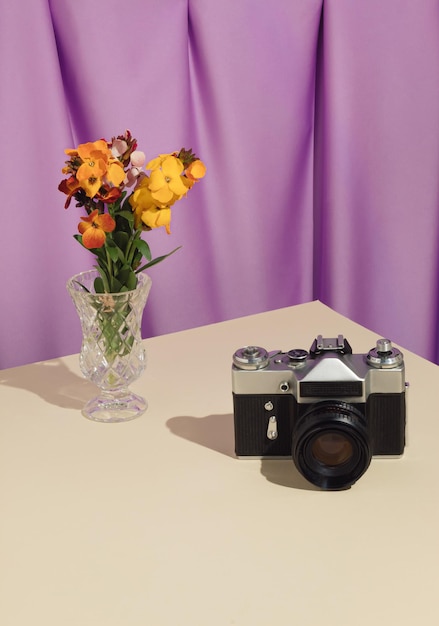 Oude retro zwarte camera met bloemen in een vaas op tafel en pastel paars gordijn Vintage concept