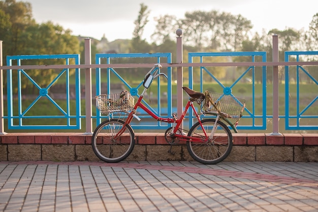 Oude rode fiets met manden bevindt zich op het hek bij zonsondergang