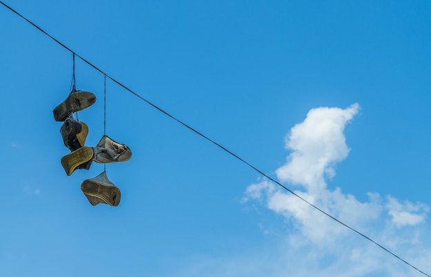 Oude schoenen die aan de hoogspanningsdraad hangen op de blauwe hemelachtergrond