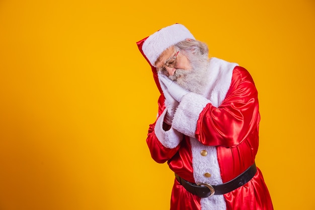 Oude senior man met grijs haar en lange baard in traditionele kerstman kostuum slapen moe dromen en poseren met de handen samen terwijl hij lacht met gesloten ogen.