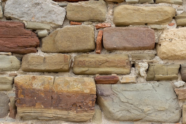 Oude stenen muur gemaakt van verschillende vierkante natuurstenen in beige, oker, rood en bruin. Stenen muur tekst