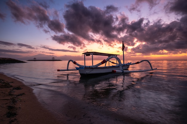 Oude traditionele Jukung-vissersboot op kust bij kleurrijke zonsopgang